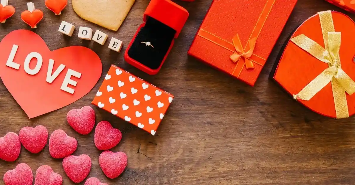 Valentine’s Day themed gifts and decorations on a wooden table, including heart-shaped cards, gift boxes, a ring box, and heart-shaped candies.