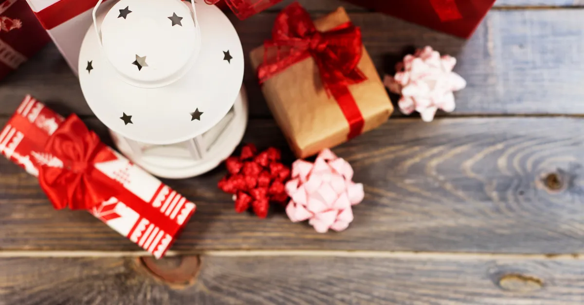Christmas gift boxes with red ribbons, decorative bows, and a white lantern placed on a wooden table.