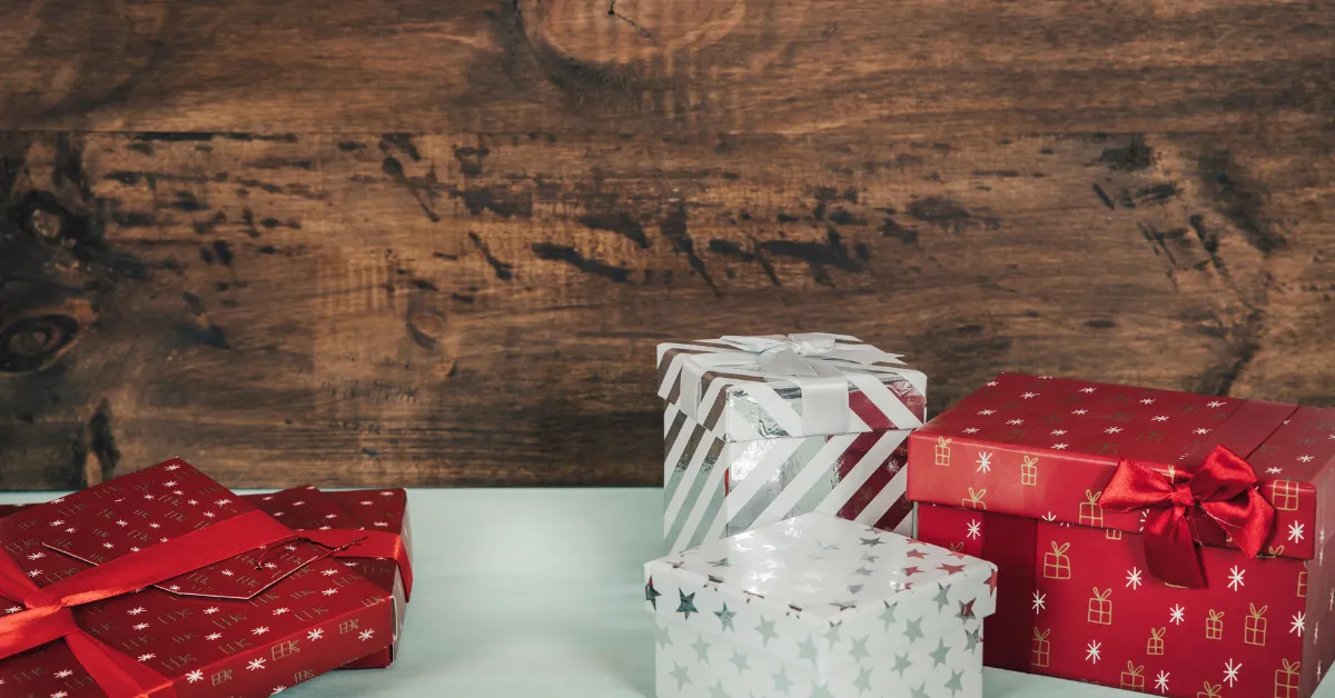 Red and white gift boxes placed on a table in front of a wooden background, decorated with ribbons and festive patterns.