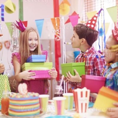 Colorful birthday party with decorated cake, balloons, gifts, and guests celebrating together.