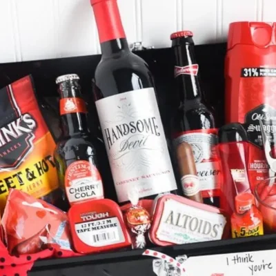 Valentine-themed gift basket for men with wine, beer, Jack Link’s beef jerky, grooming products, candy, and small accessories arranged in a black tray with red decorations.