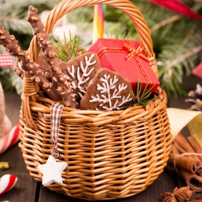 Christmas gift basket with gingerbread cookies, chocolate sticks, candy canes, and a small wrapped present surrounded by pine branches and holiday decorations.